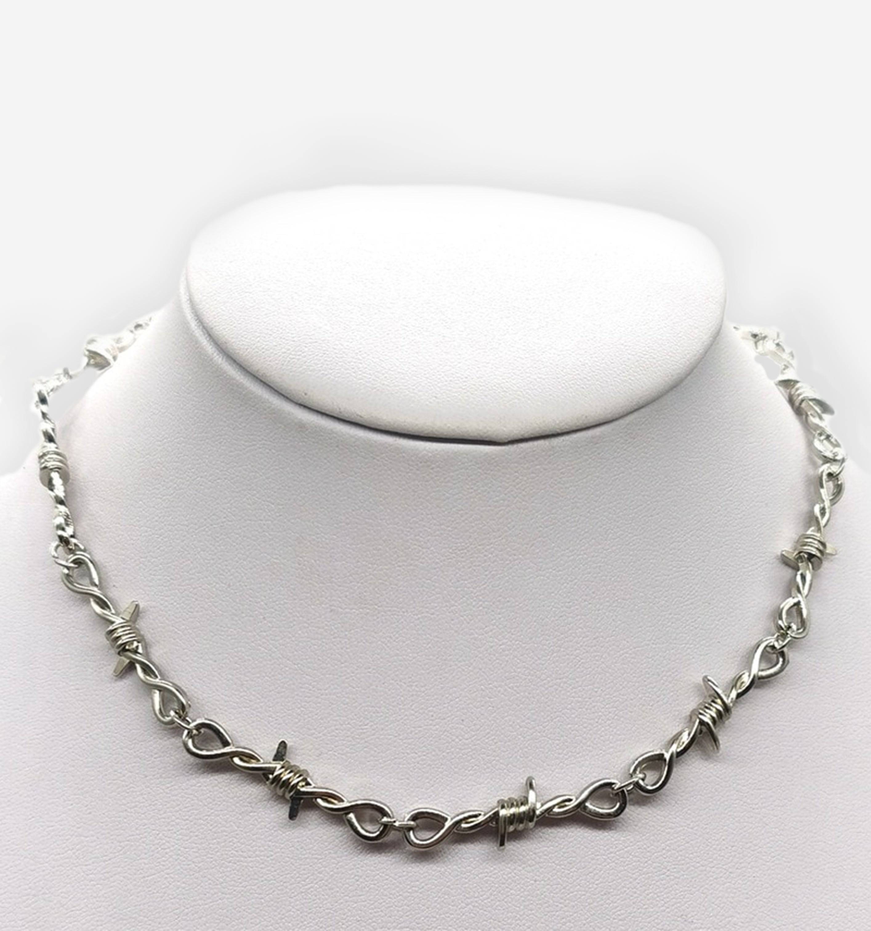 Black barbed necklace by 2KWRLD featuring metal spikes and a chain design, displayed on a neutral background.