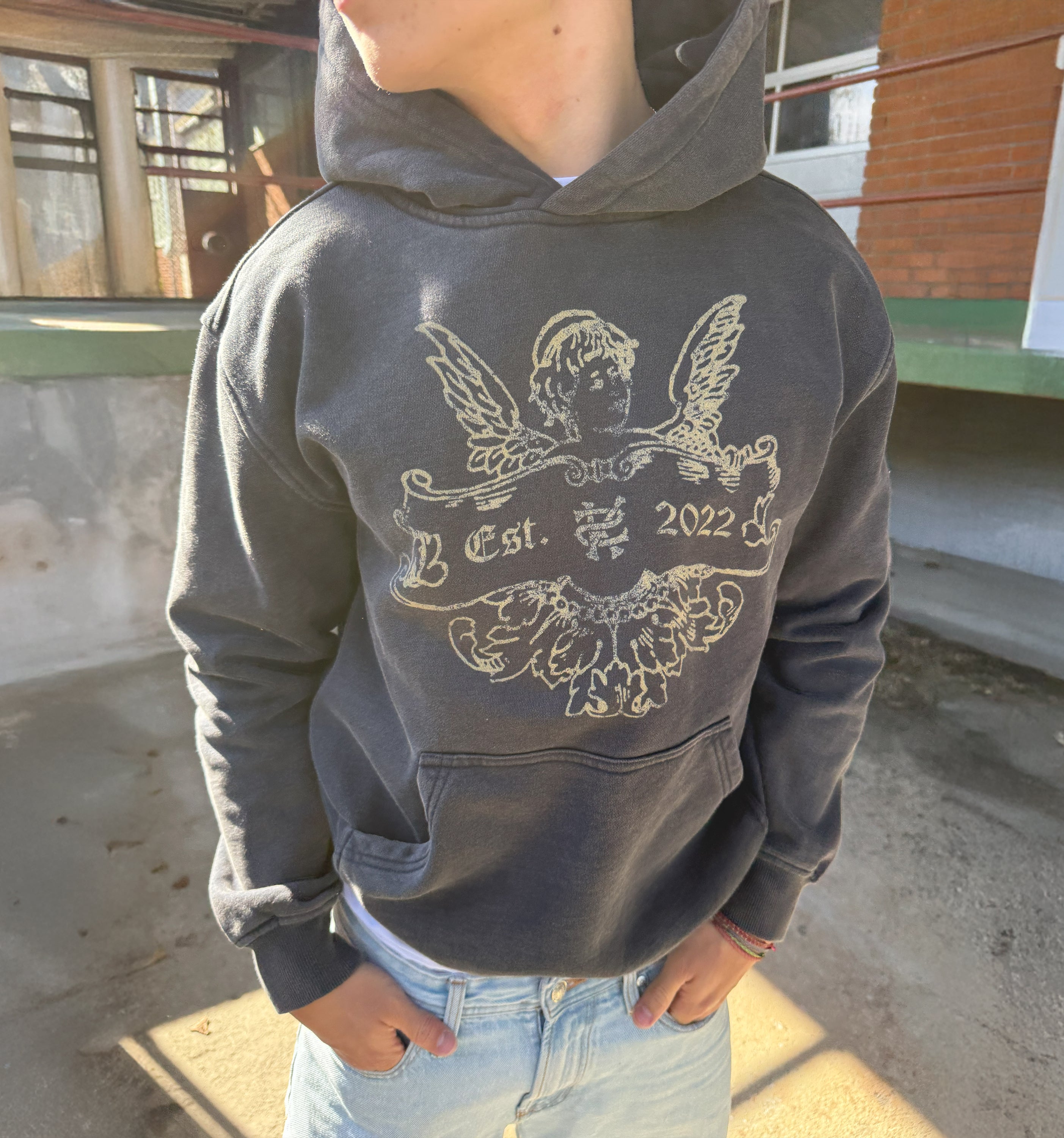 Coming Soon 2K WRLD branded hoodie worn by a person, showcasing a casual streetwear style with graphic design on the front.